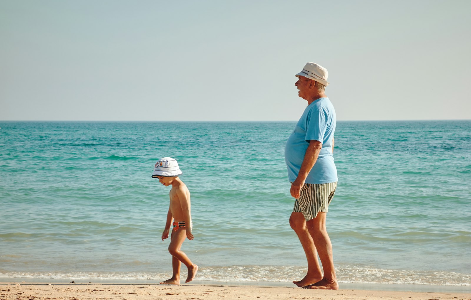 A grandparent and child walking together along the shoreline