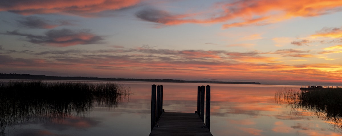 An empty wooden dock reaching into a still lake at dawn