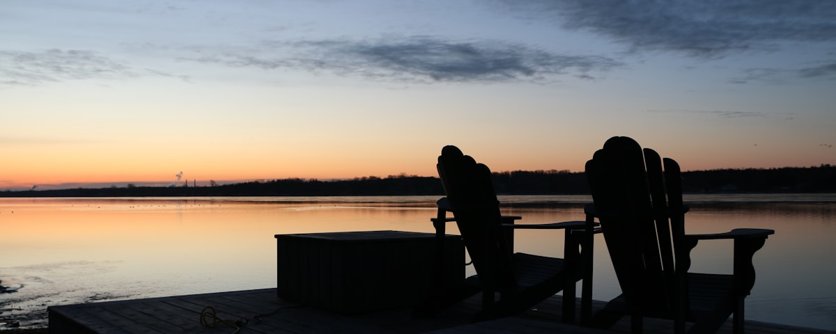 Two wooden chairs on a lakeside dock at dusk