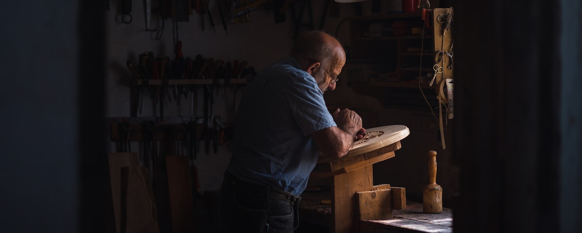 A craftsman shaping wood at a workbench in warm workshop light