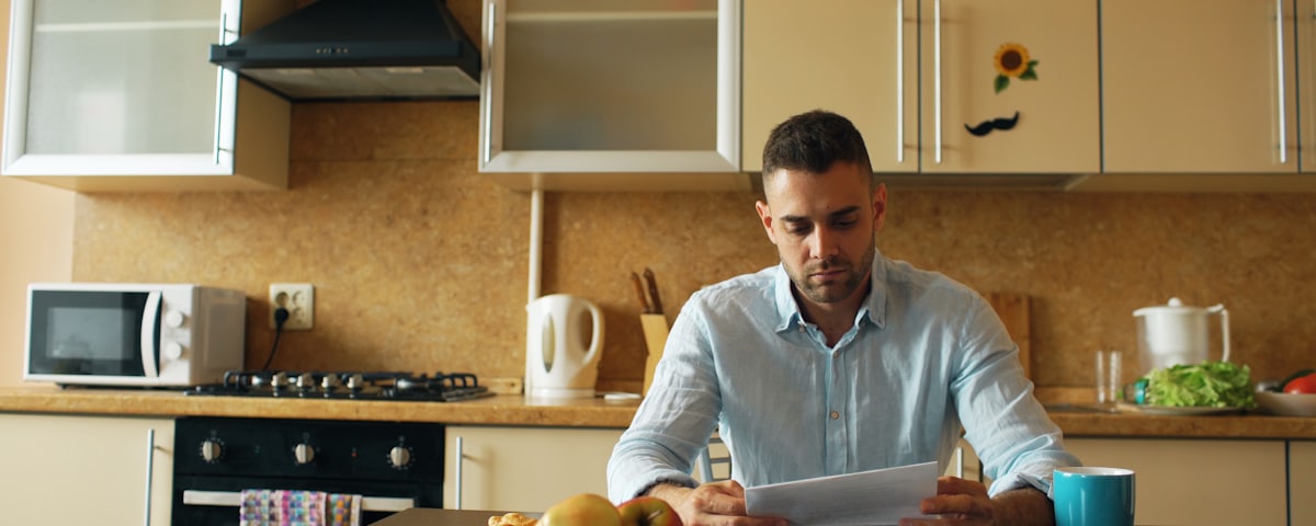 A person reading a document at a kitchen table in morning light